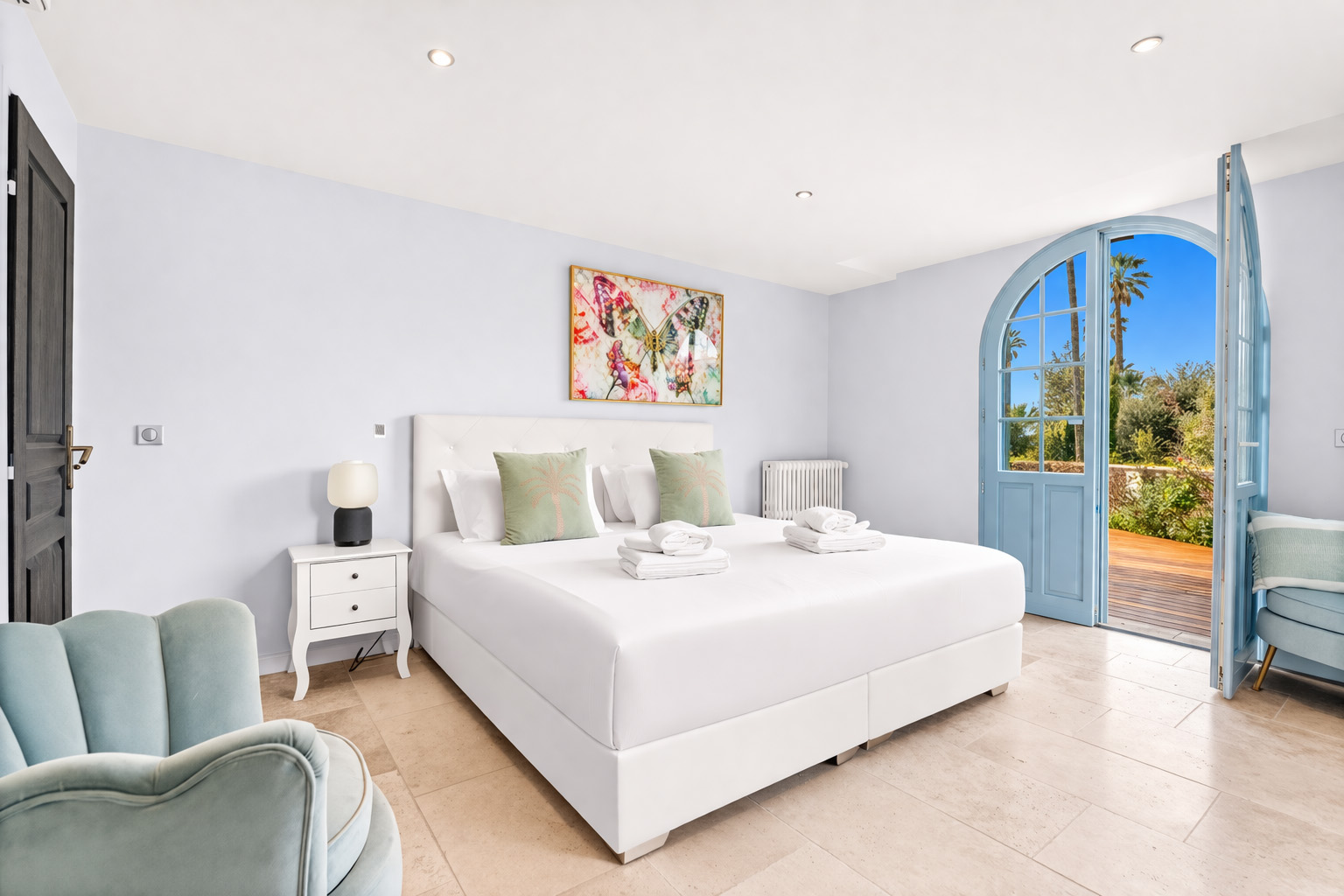 bright-bedroom-suite-blue-arched-door-cannes Elegant guest bedroom with balcony doors, fireplace and luxury furnishings at Château Les Alouettes Cannes.